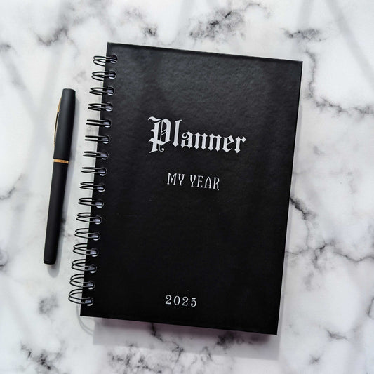 A 2025 Gothic Planner with a black hardback cover that says Planner, My Year and 2025 on the front in white.